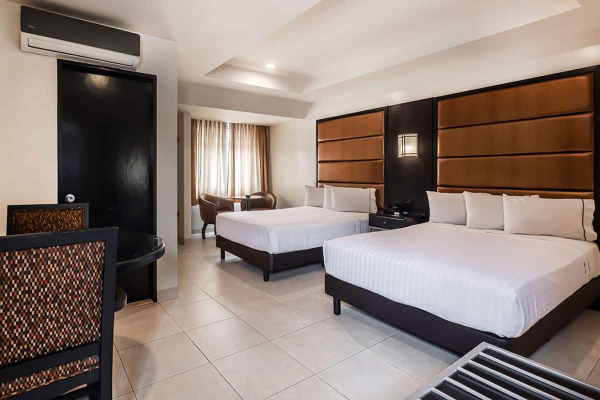 A hotel room with two beds, a seating area with chairs, a small table, and a wall-mounted air conditioning unit.