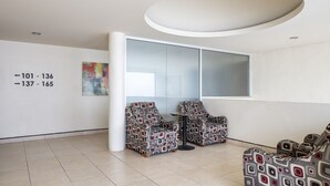 Un espace d’attente moderne, doté de deux fauteuils à motifs, d’une grande fenêtre et d’un mur orné de panneaux de signalisation.