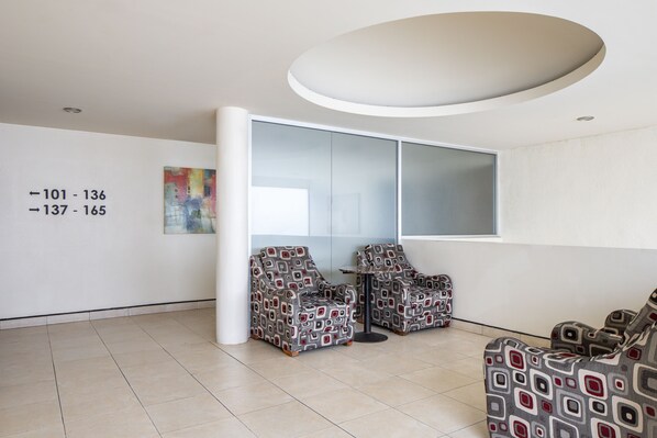 A modern waiting area with two patterned chairs, a large window, and a wall with directional signs.