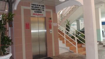 An elevator with a sign in Spanish, a staircase, and a potted plant.