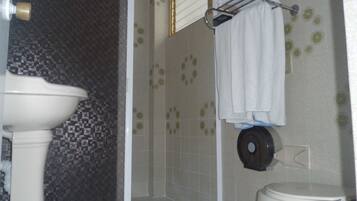 Un baño con lavamanos blanco, inodoro y zona de ducha con puerta de cristal.
