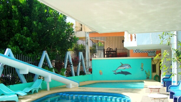 Une piscine ornée d’une fresque représentant des dauphins, avec un toboggan et des chaises longues.