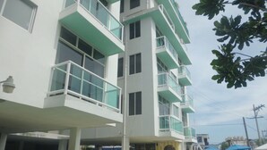 Un hôtel à plusieurs étages doté de balcons, d’un espace piscine avec des chaises longues et d’un espace détente abrité.