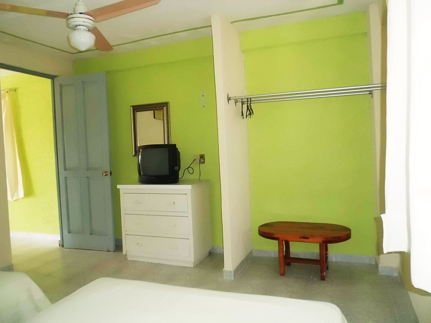 Un dormitorio con cama, cómoda, televisor encima, espejo y ventilador de techo.