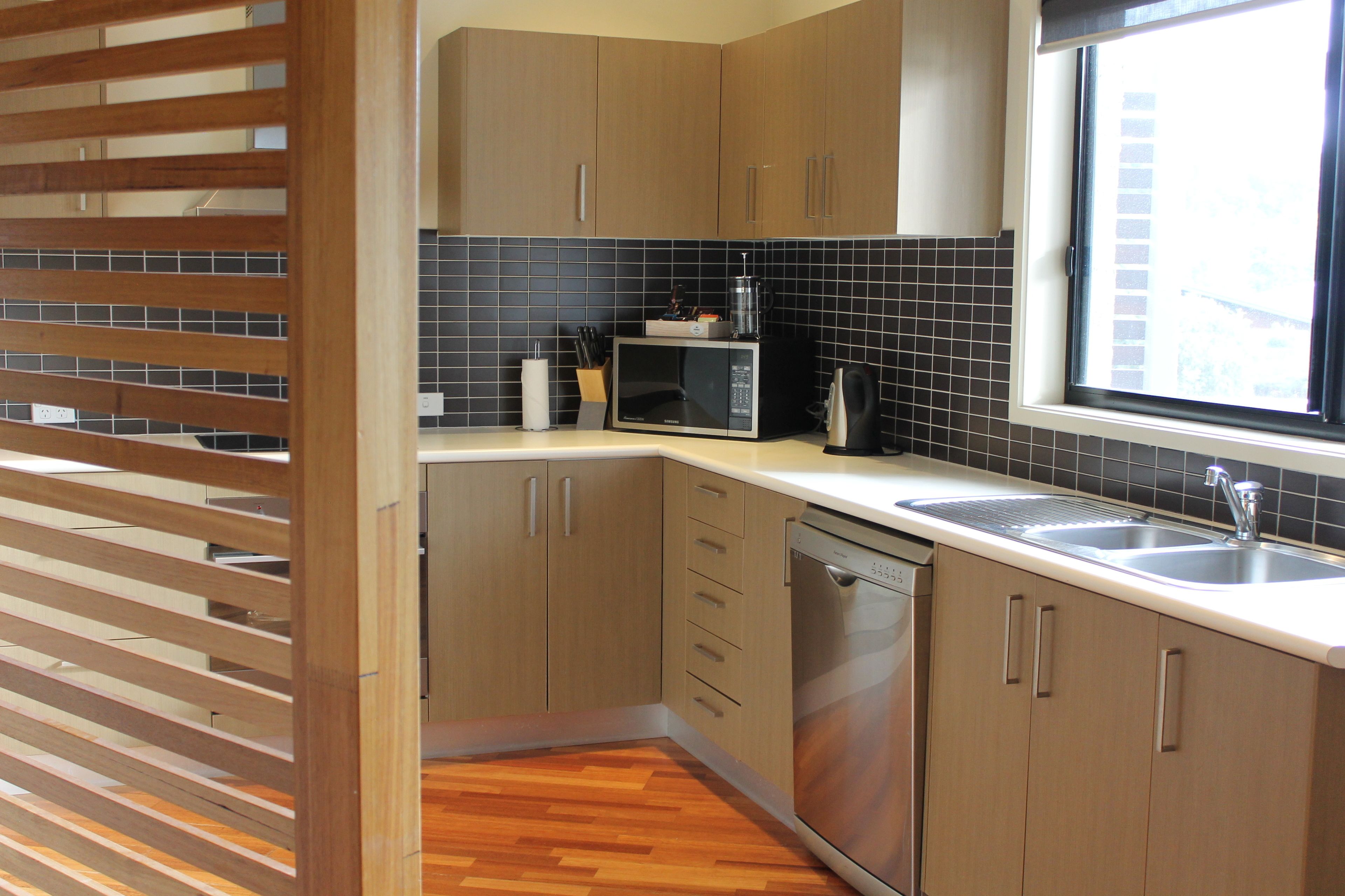 A modern kitchen with wooden cabinets, a microwave, a dishwasher, and a window with a view of the city.