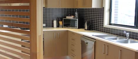 A modern kitchen with wooden cabinets, a microwave, a dishwasher, and a window with a view of the city.