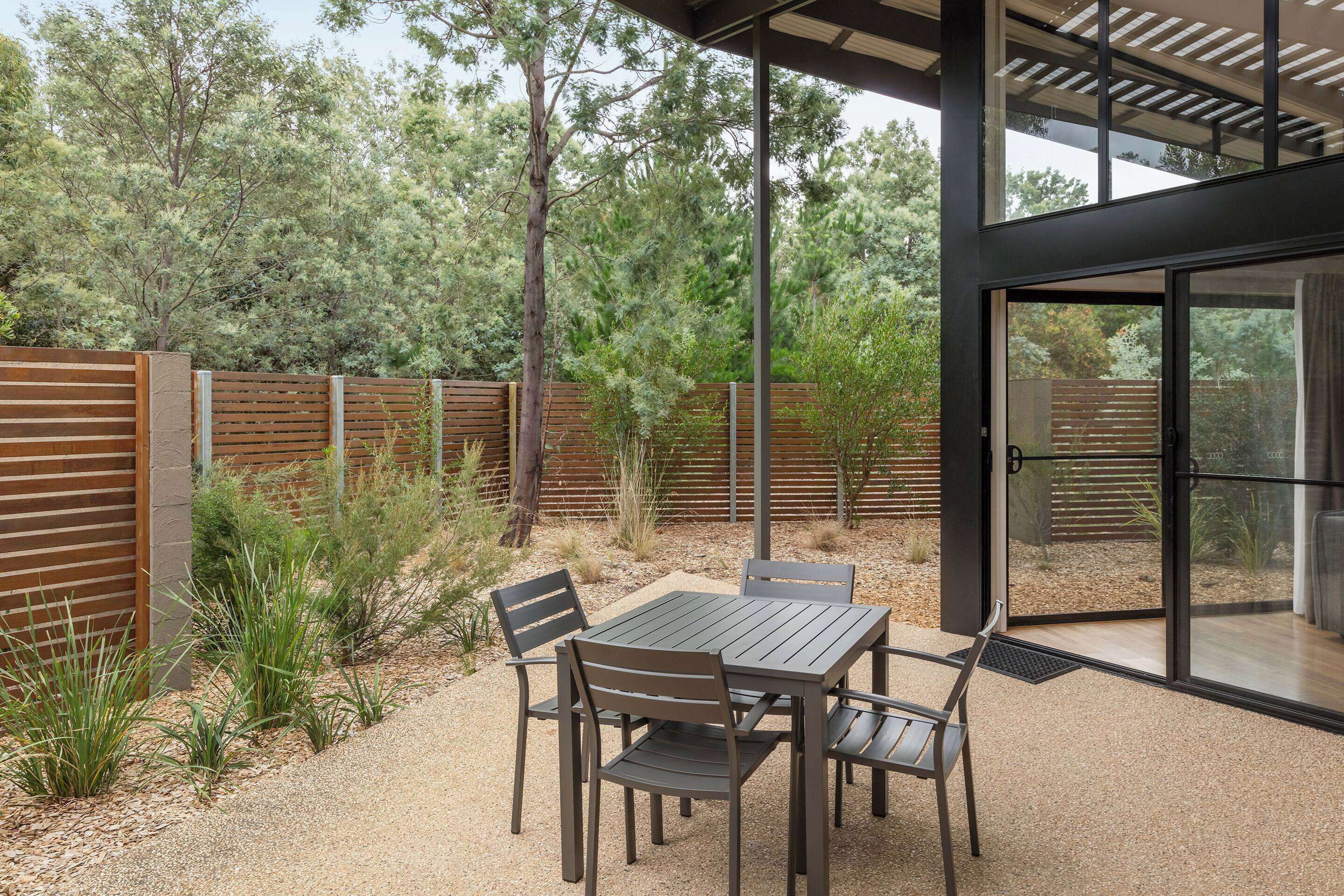 Une terrasse avec une table et des chaises, entourée d’une clôture en bois et de plantes.