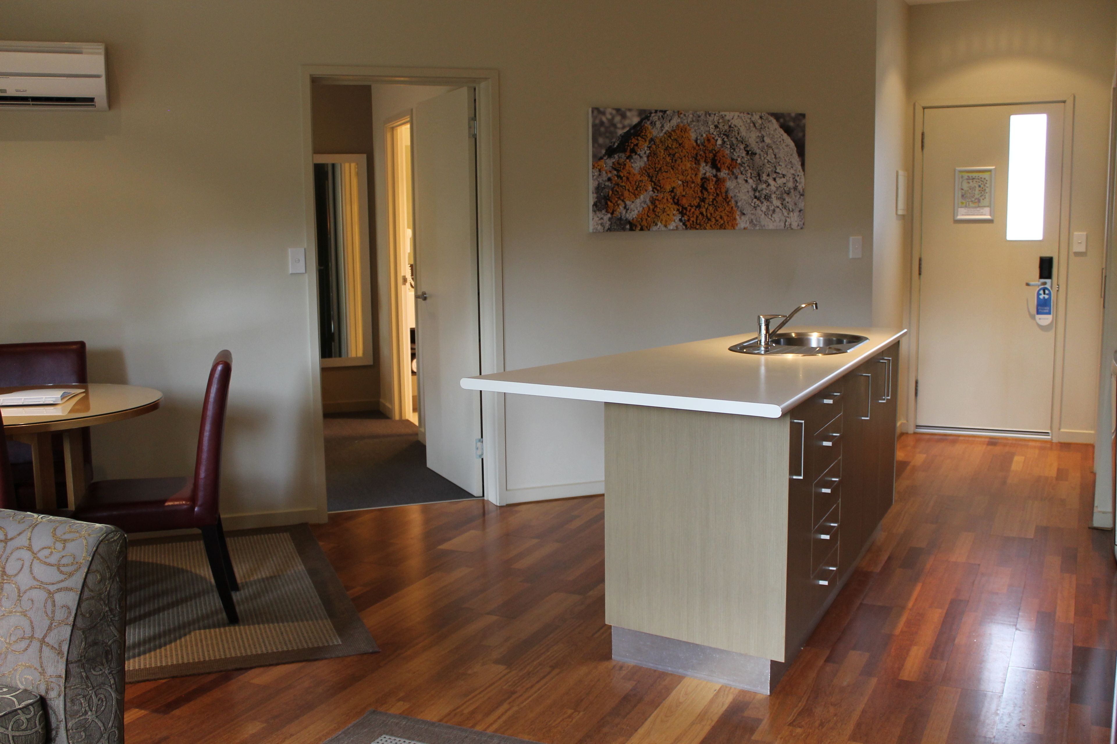 A compact kitchen with a white countertop, a built-in sink, and a small dining area with a chair and table.