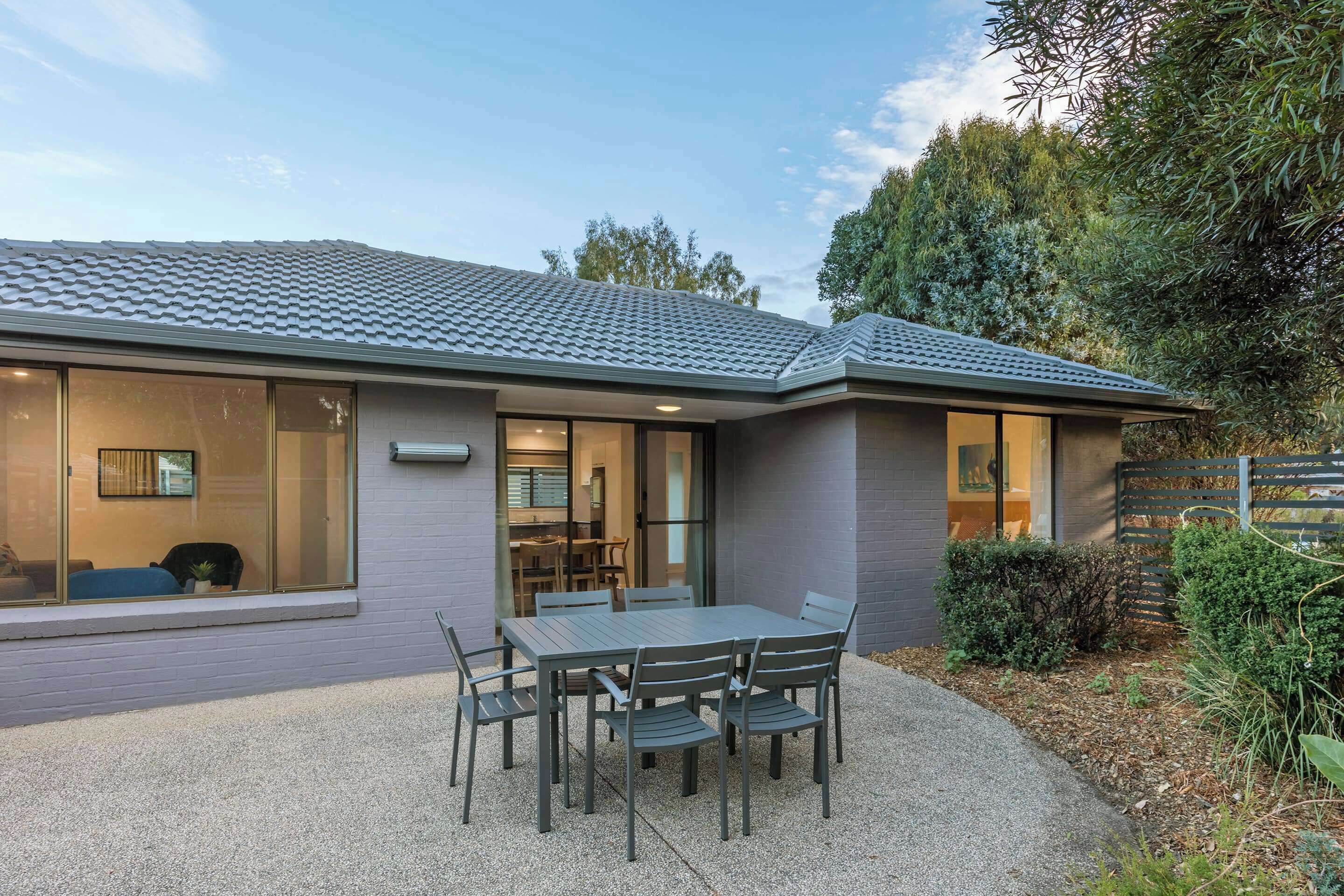 Une maison moderne dotée d’un patio, d’une table à manger avec des chaises et d’un espace extérieur couvert.