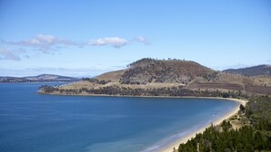 A coastal landscape with a beach, a hill with sparse vegetation, and a clear blue sky.