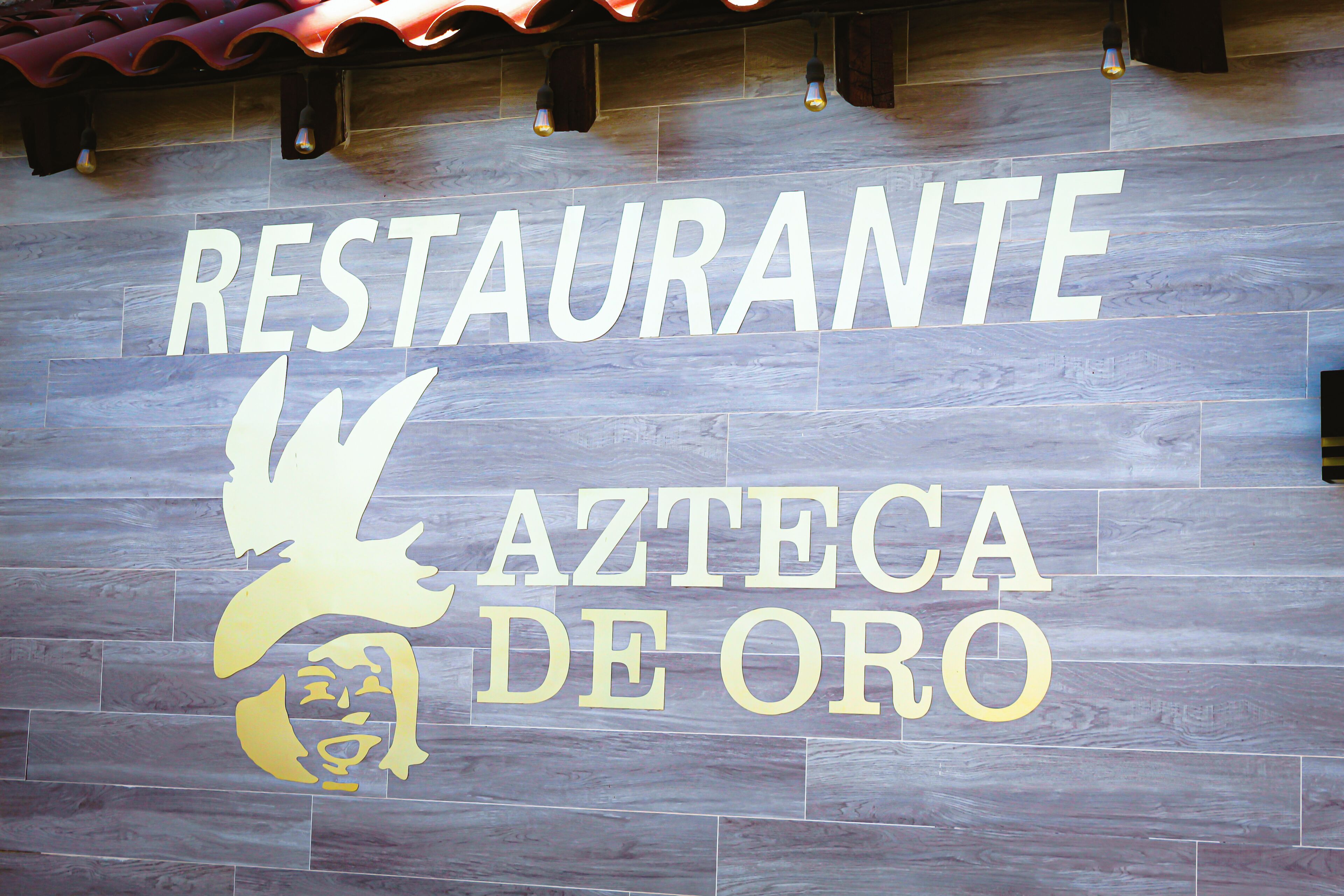 Letrero de restaurante con la leyenda 'RESTAURANTE AZTECA DE ORO' y un logotipo de águila dorada.