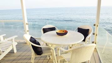 Una mesa redonda con cuatro sillas blancas de mimbre, un frutero y vista al mar.