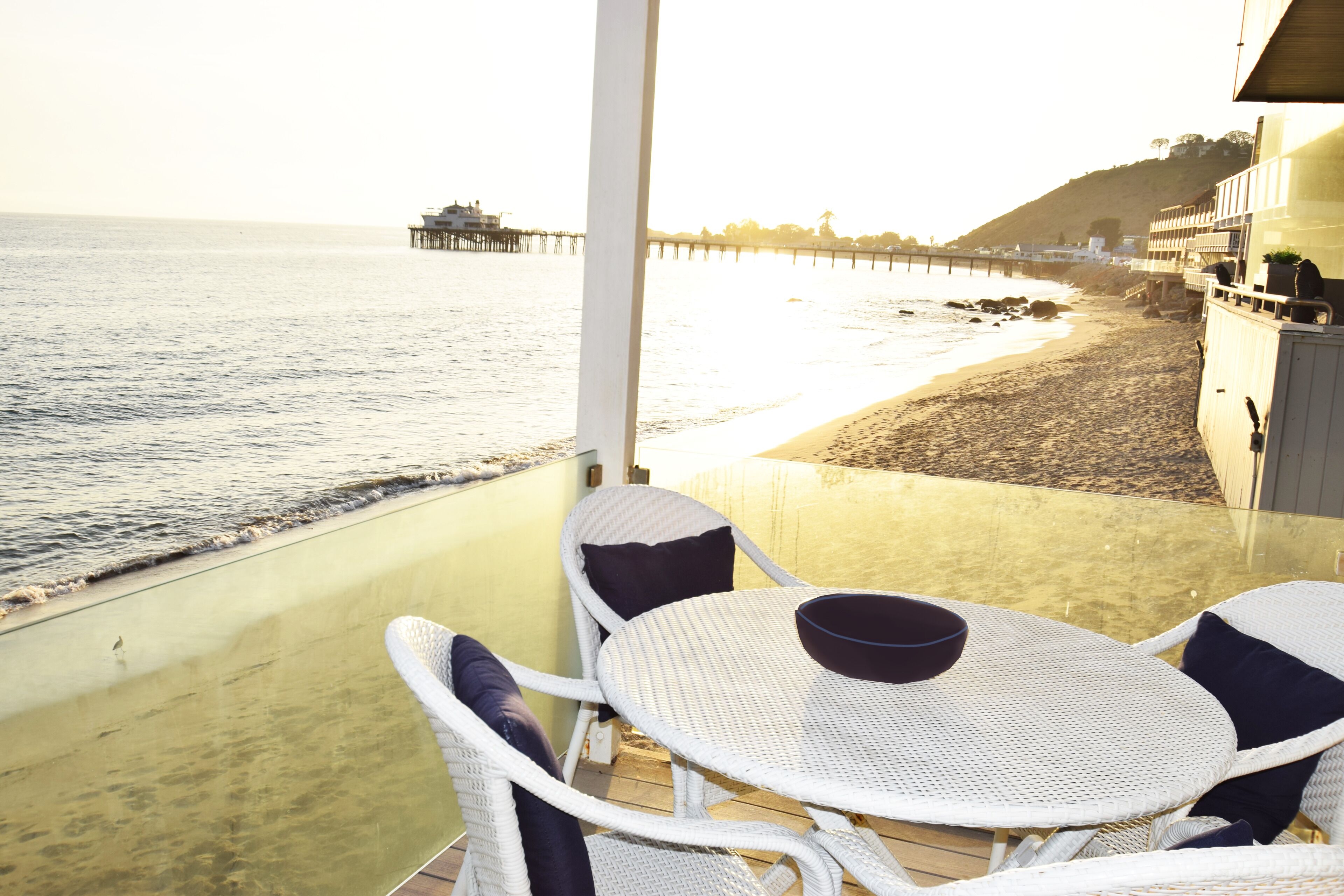 Een balkon met uitzicht op het strand en de oceaan. Er staat een tafel met stoelen en een schaal op.