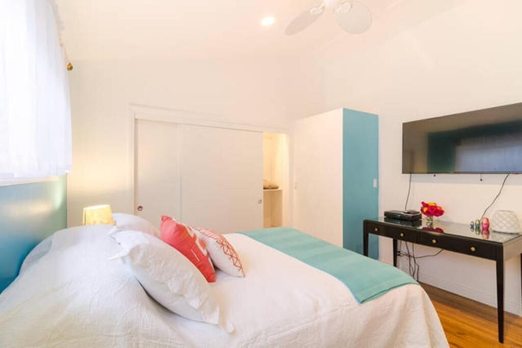 A bedroom with a bed, a desk, a TV, and a door.