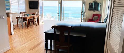 Una habitación con piso de madera, una cama, un área de comedor con sillas, una mesa y vista al océano a través de amplios ventanales.