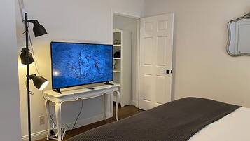 Ett sovrum med en säng, en tv på ett vitt stativ, en golvlampa och en dörr till en garderob.