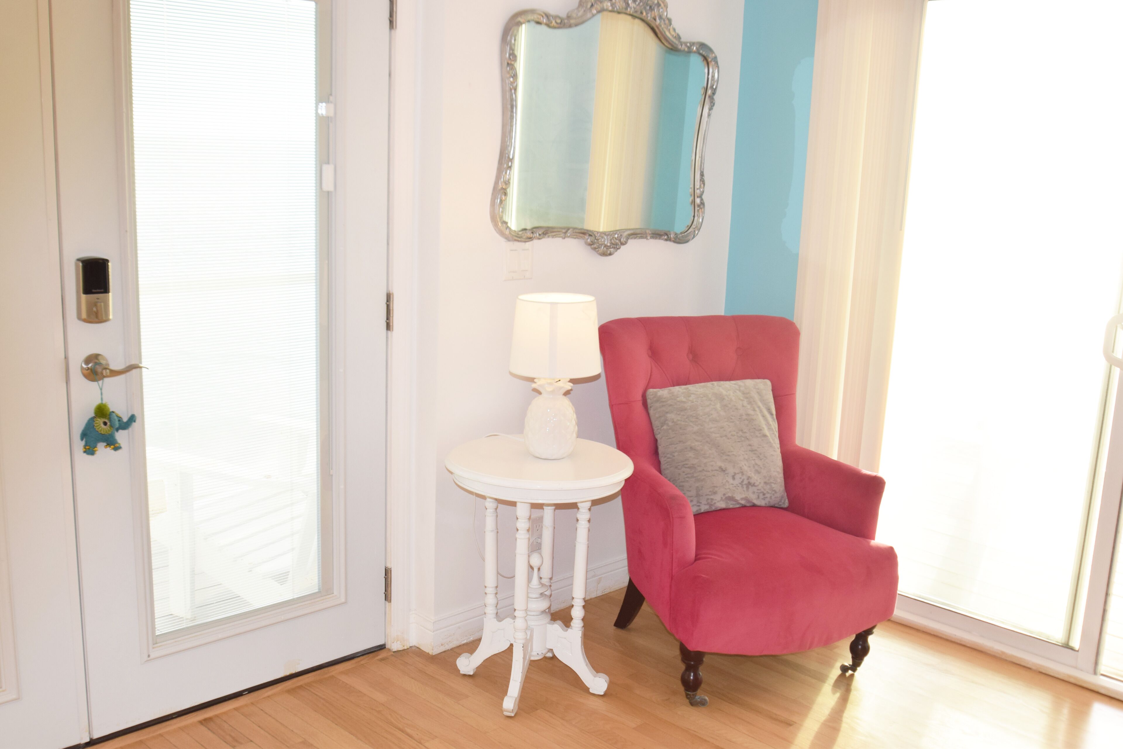 A room with a red armchair, a small white table with a lamp, a mirror, and a door with a lock.