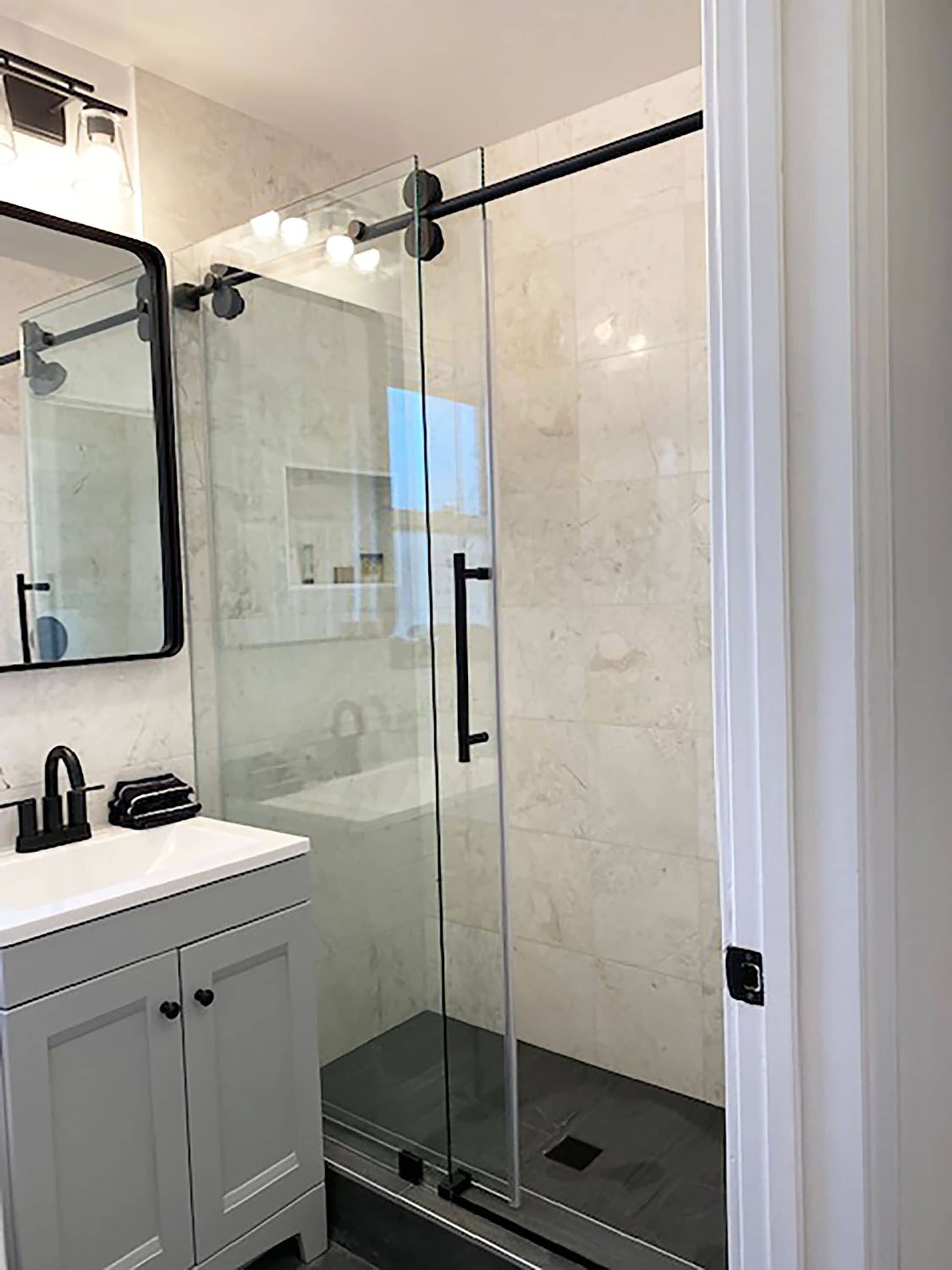 A modern bathroom with a glass shower enclosure, a white sink with a black faucet, and a large mirror above the sink.