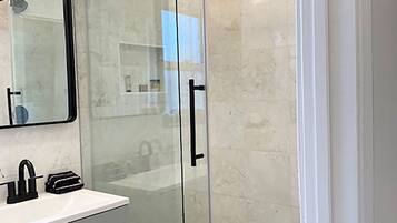 A modern bathroom with a glass shower enclosure, a white sink with a black faucet, and a large mirror above the sink.