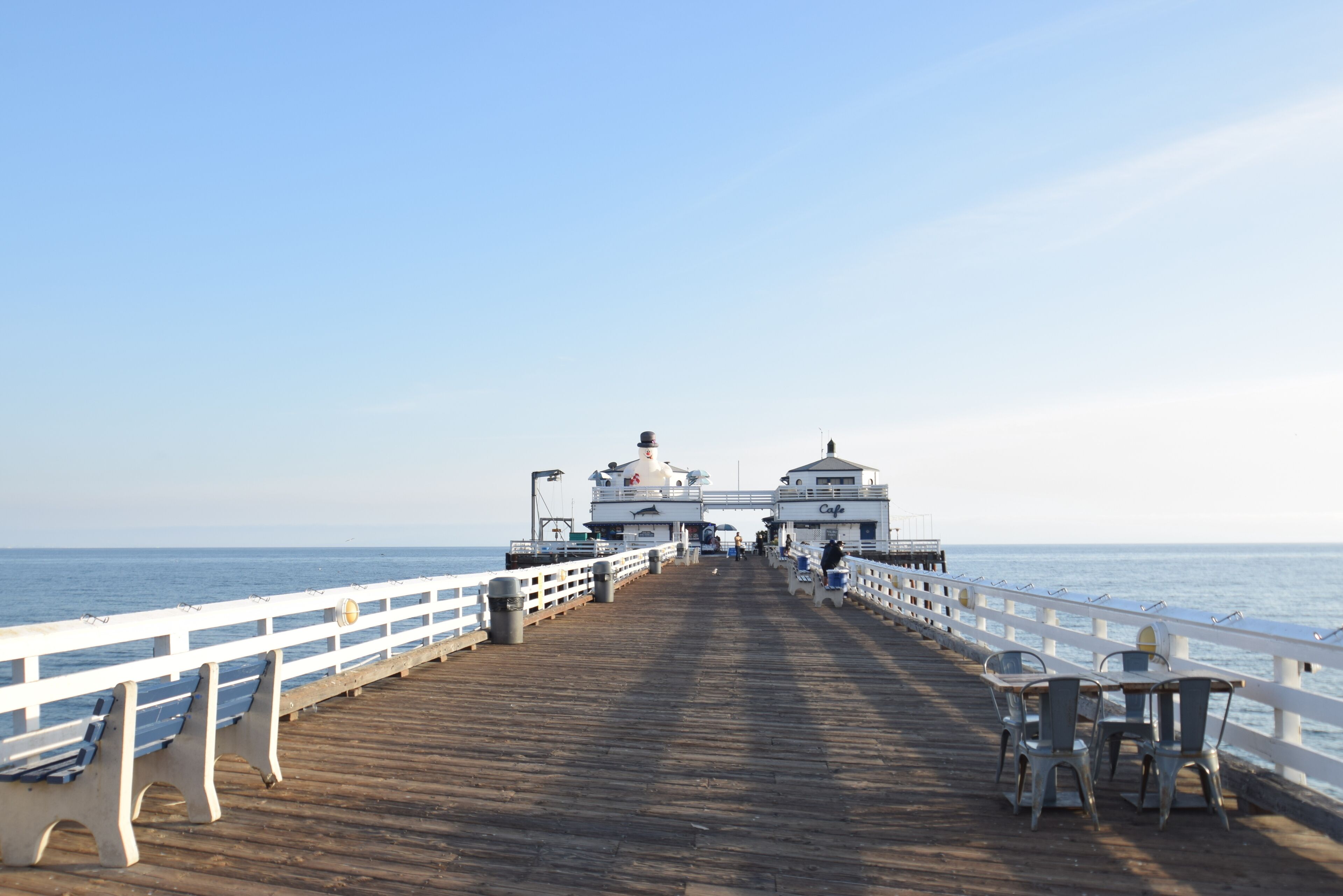 A pier with benches and tables, leading to a building with a dome and a sign that reads "Cafe."