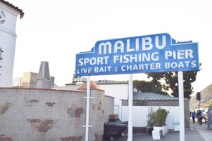 A sign for Malibu Sport Fishing Pier advertising live bait and charter boats.