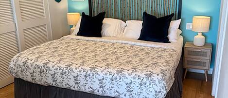 Un dormitorio con una cama grande, un cabecero con líneas verticales, dos mesitas de noche con lámparas y una puerta con persianas.