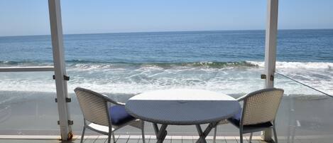 Un espace extérieur abrité, avec une table et deux chaises, offrant une vue sur l’océan.