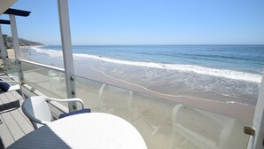 Un balcon doté de chaises en osier blanc, donnant sur une plage aux vagues douces.