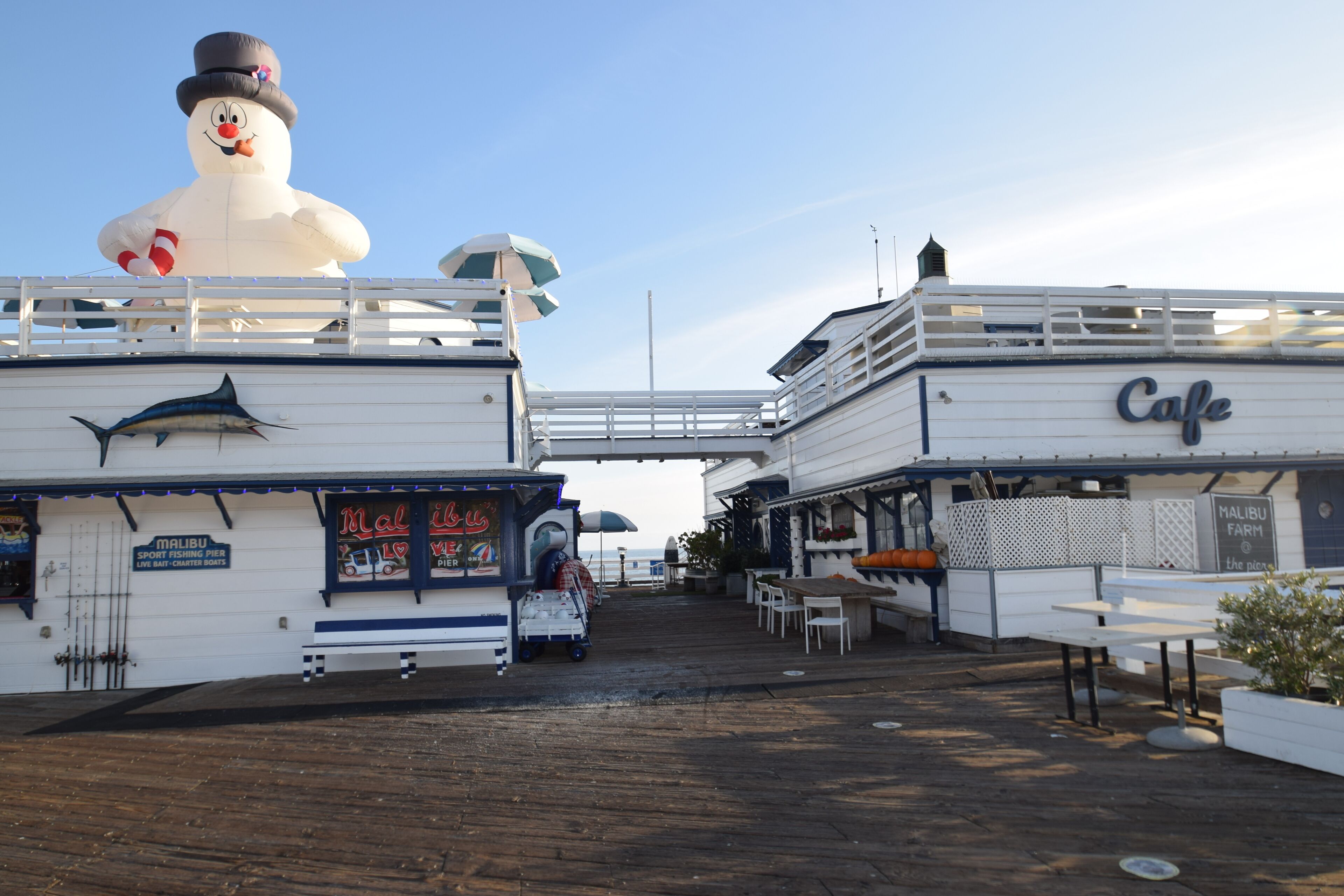 Un restaurant situé au bord de l’eau, agrémenté d’un grand bonhomme de neige décoratif, doté d’une terrasse et d’un panneau indiquant la direction du ponton de Malibu.