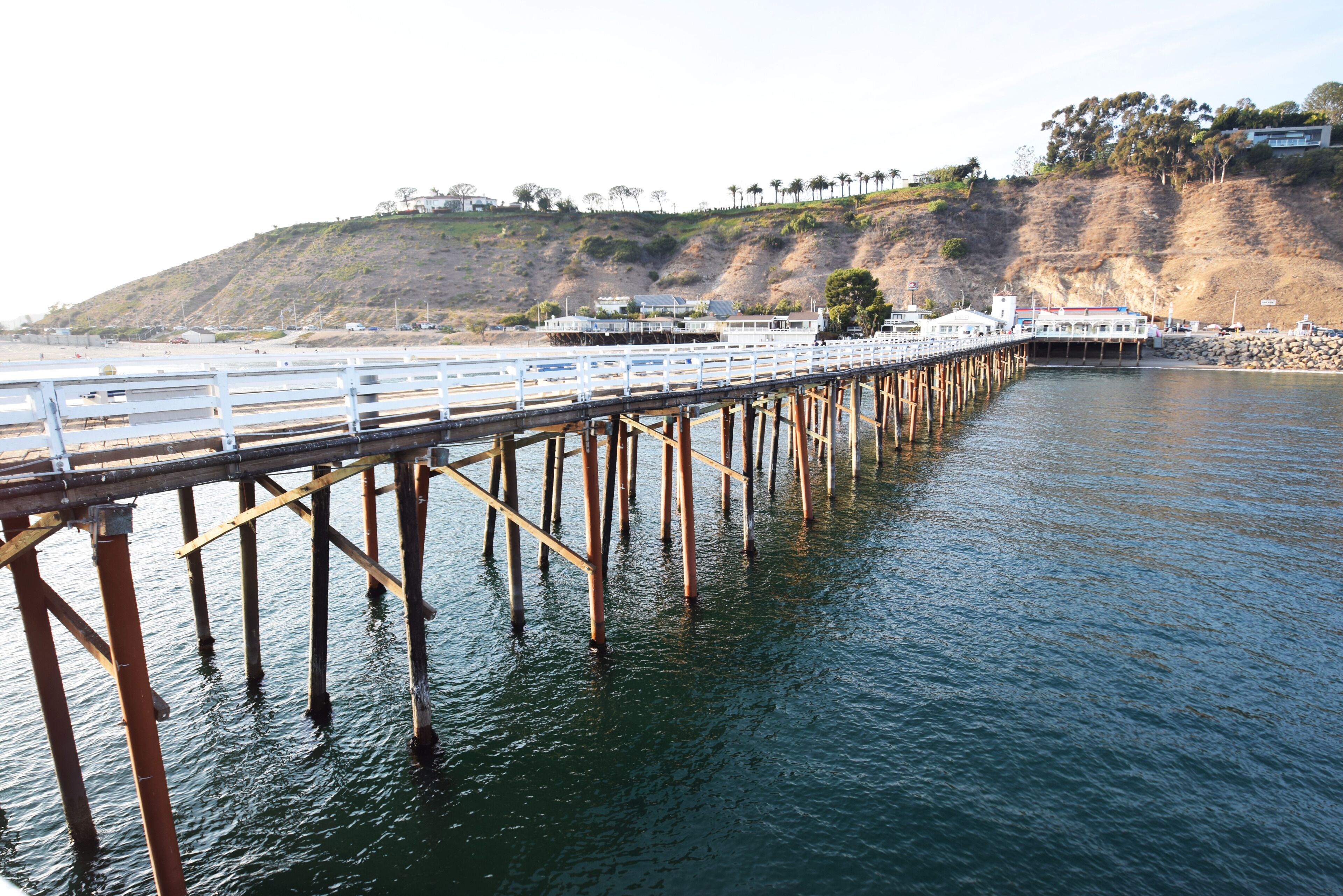 A pier extending into calm water with a hillside in the background.