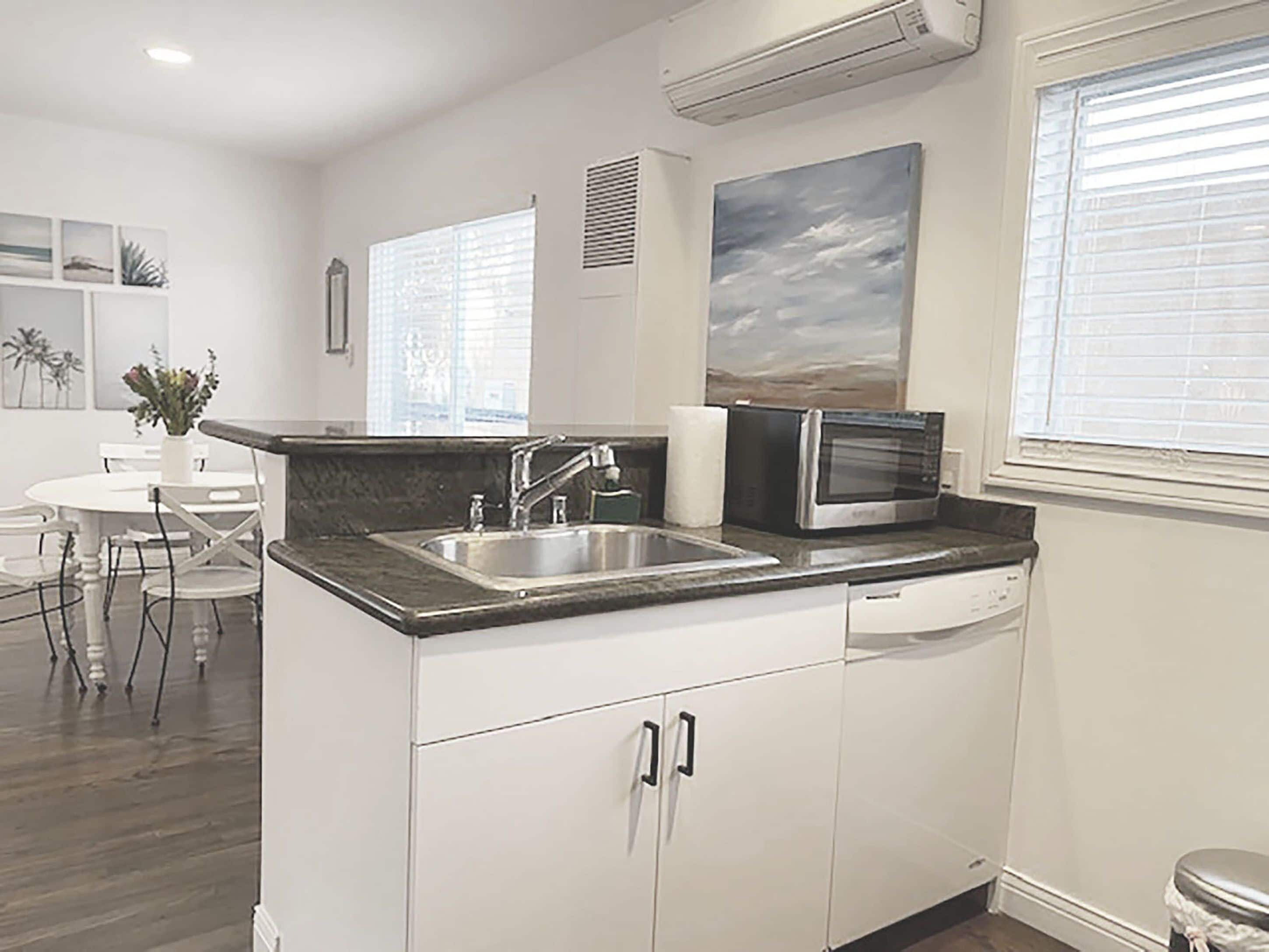 A modern kitchen with white cabinets, a stainless steel sink, a microwave, and a window with blinds.
