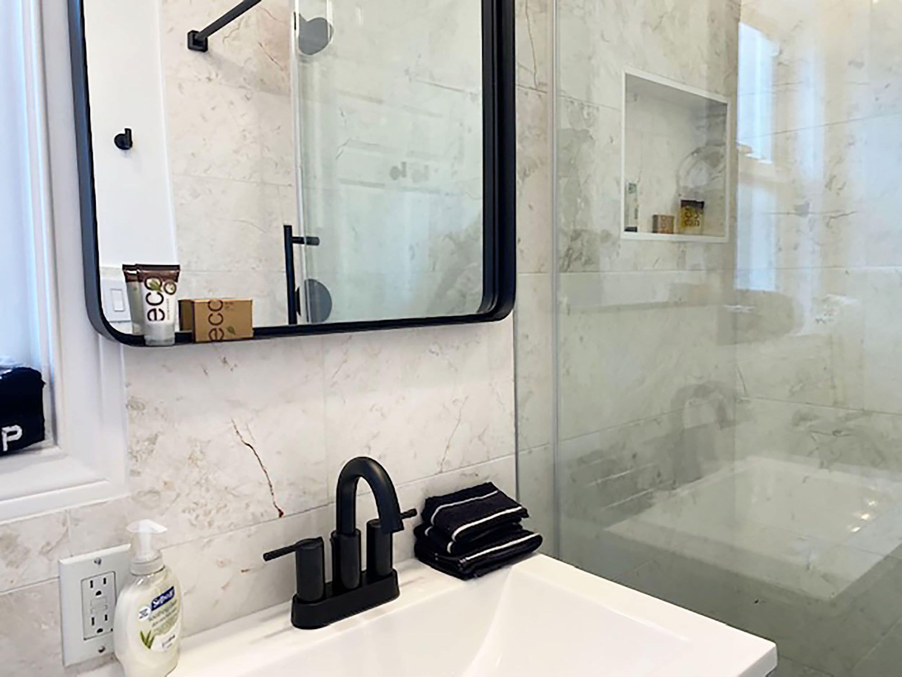 Une salle de bain avec un lavabo blanc, un robinet noir et un miroir au-dessus. Un flacon de savon liquide se trouve sur le côté gauche du lavabo.
