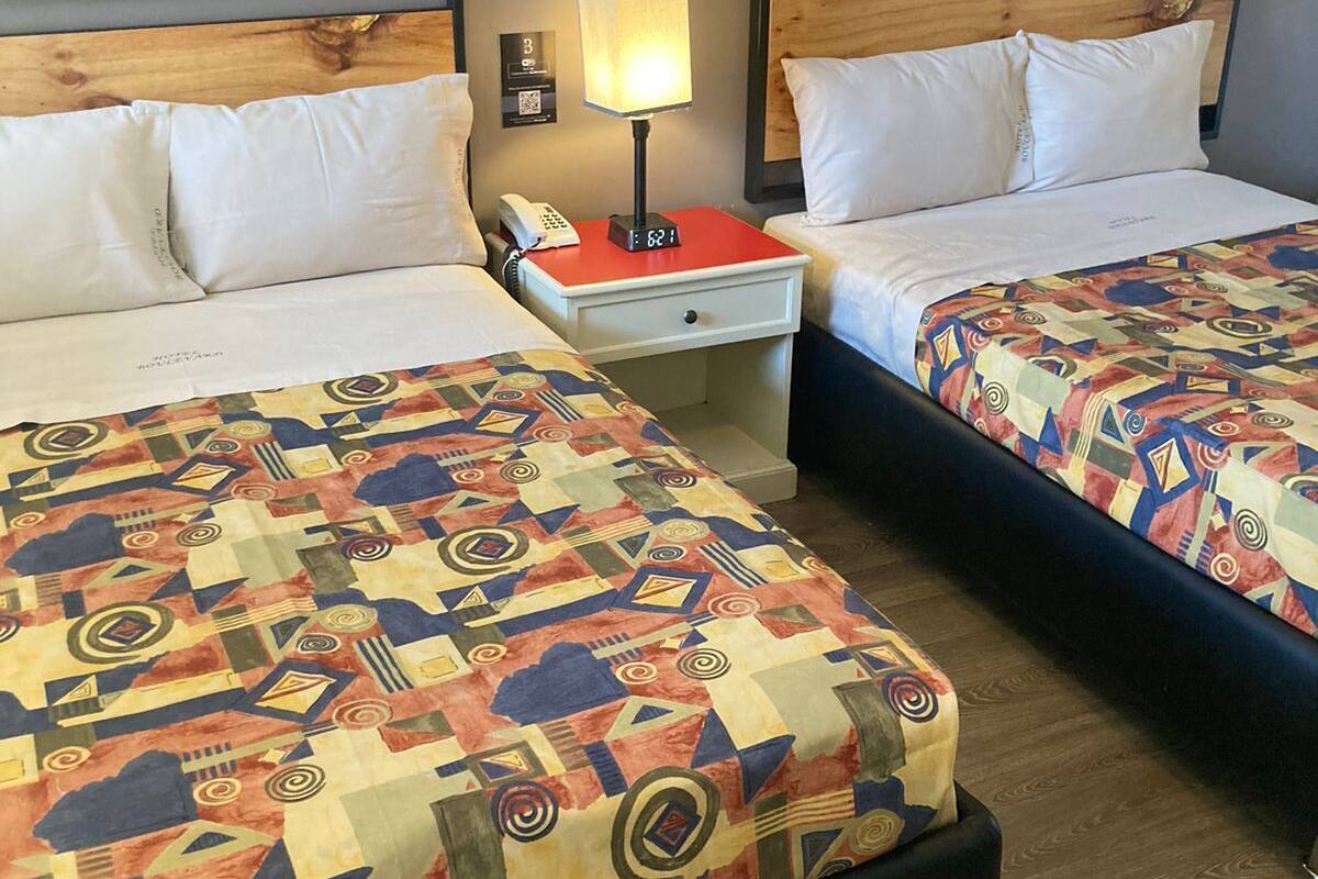 Quarto de hotel com duas camas, uma mesinha de cabeceira com abajur, telefone e relógio de parede.