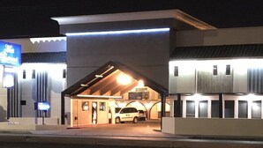 Een hotel met modern design, herkenbaar aan een opvallende ingang, een parkeerplaats en een bord met faciliteiten.