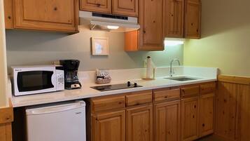 Una cocina con armarios de madera, microondas, cafetera, lavamanos y refrigerador.