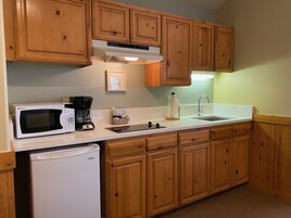 Una cocina con armarios de madera, microondas, cafetera, lavamanos y refrigerador.