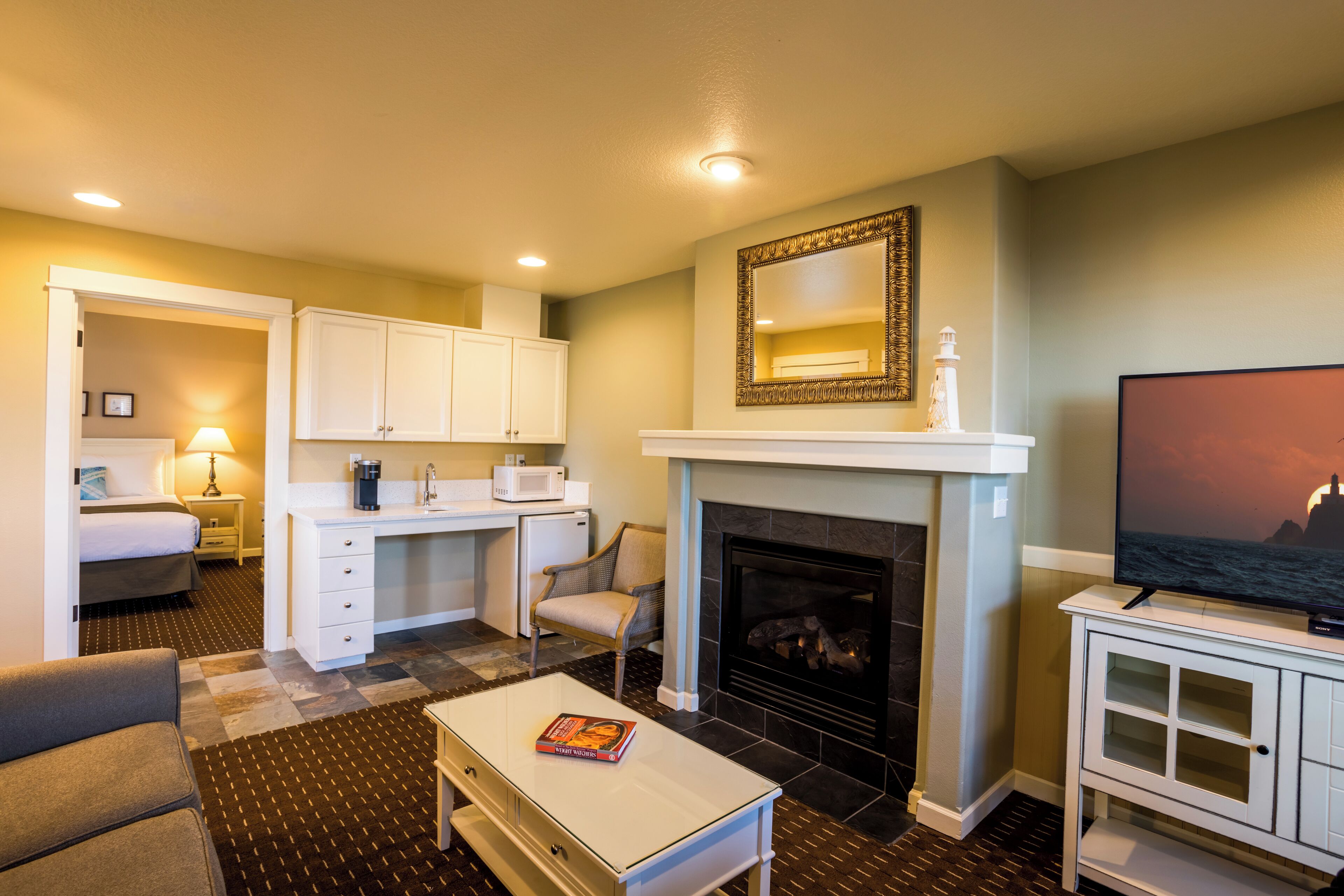 A hotel room with a bed, a desk, a fireplace, a TV, and a view of the ocean.