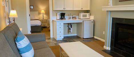 A compact living space with a kitchenette, a sofa with a blue pillow, a coffee table, a bed, and a fireplace.