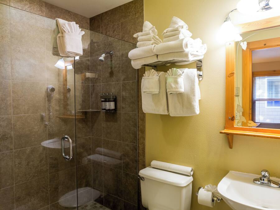 A bathroom with a glass-enclosed shower, a toilet, a sink, and multiple towels neatly arranged on a rack.