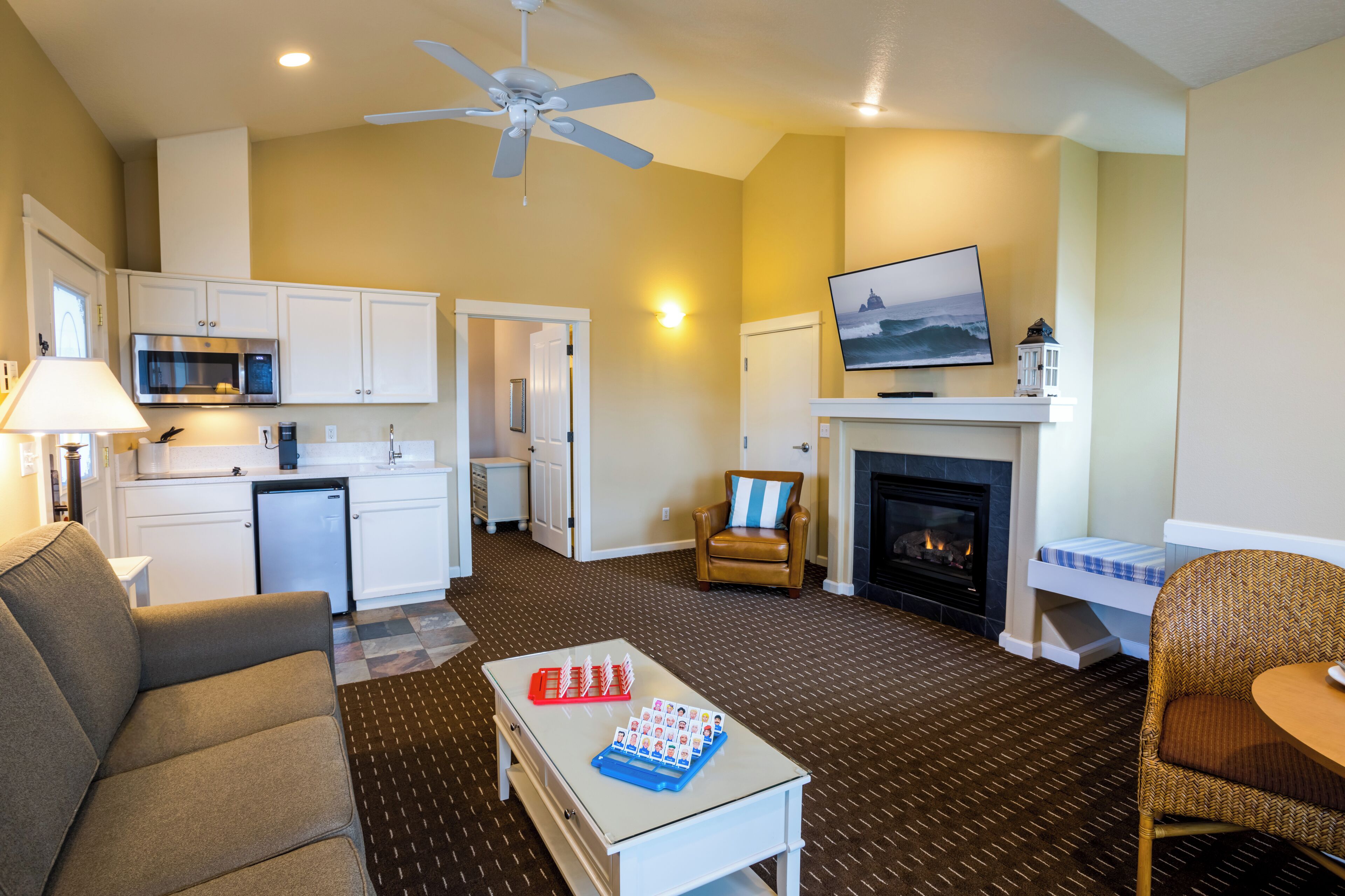 A living room with a sofa, a coffee table, a fireplace, a television, and a kitchen area with cabinets and a microwave.