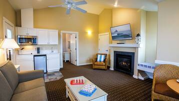 A living room with a sofa, a coffee table, a fireplace, a television, and a kitchen area with cabinets and a microwave.
