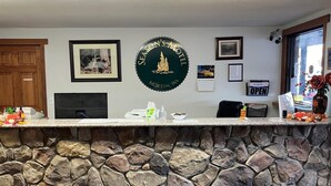 Un área de recepción con una pared de piedra, un cartel enmarcado de Season's Motel, un mostrador con una computadora y varios objetos sobre él.