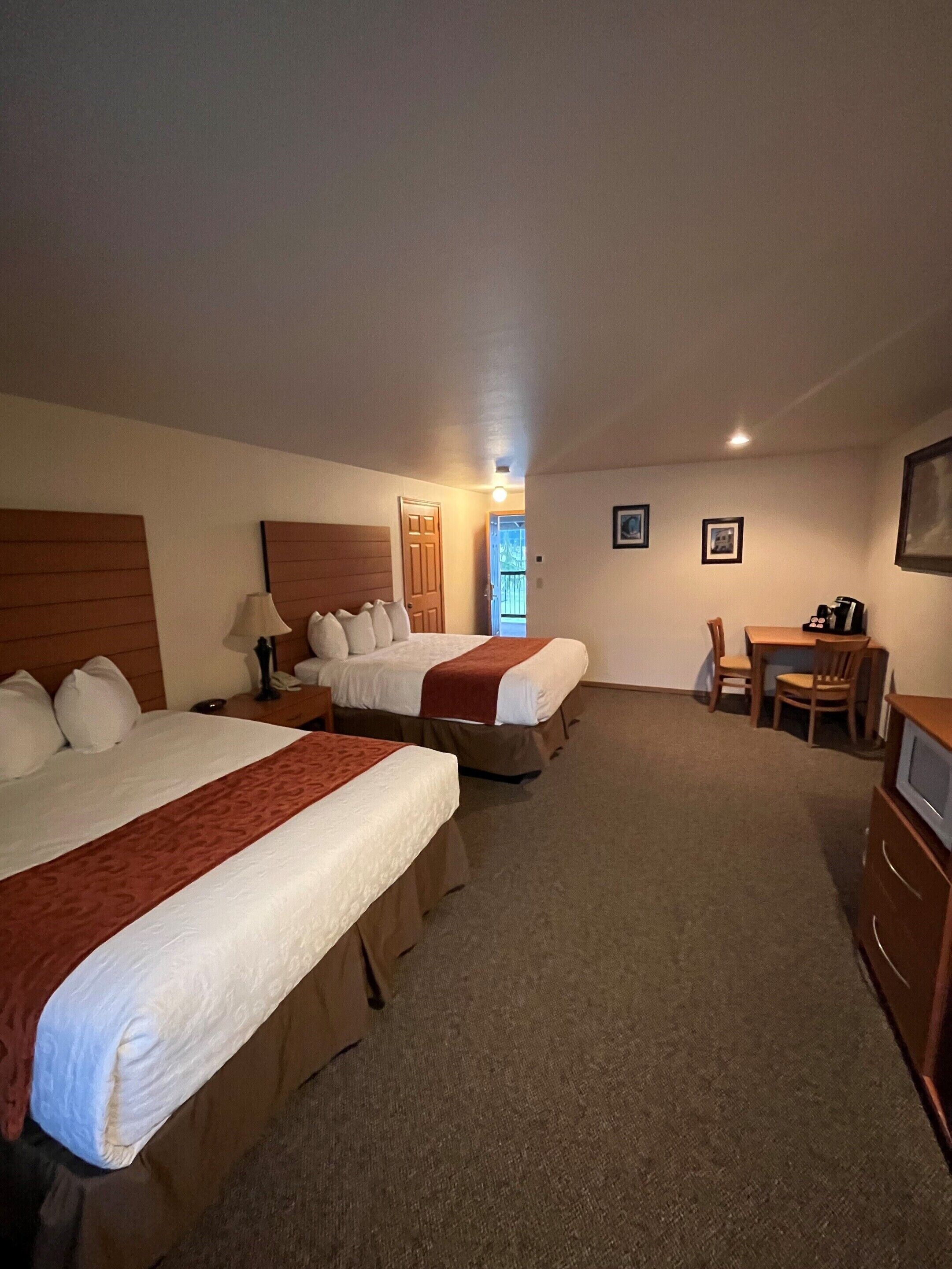A hotel room with two beds, a desk, a chair, a television, and a door leading to a balcony.