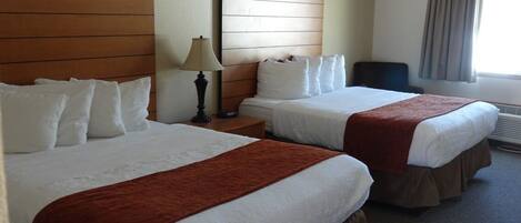 A hotel room with two beds, a nightstand, a lamp, a chair, and a window with curtains.
