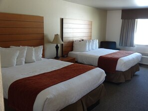 A hotel room with two beds, a nightstand, a lamp, a chair, and a window with curtains.