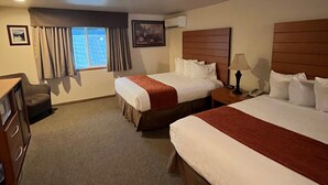 Una habitación de hotel con dos camas, un escritorio, una silla y un ventanal con cortinas.