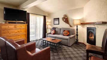 A living room with a sofa, armchairs, a coffee table, a television, a fireplace, and a lamp.