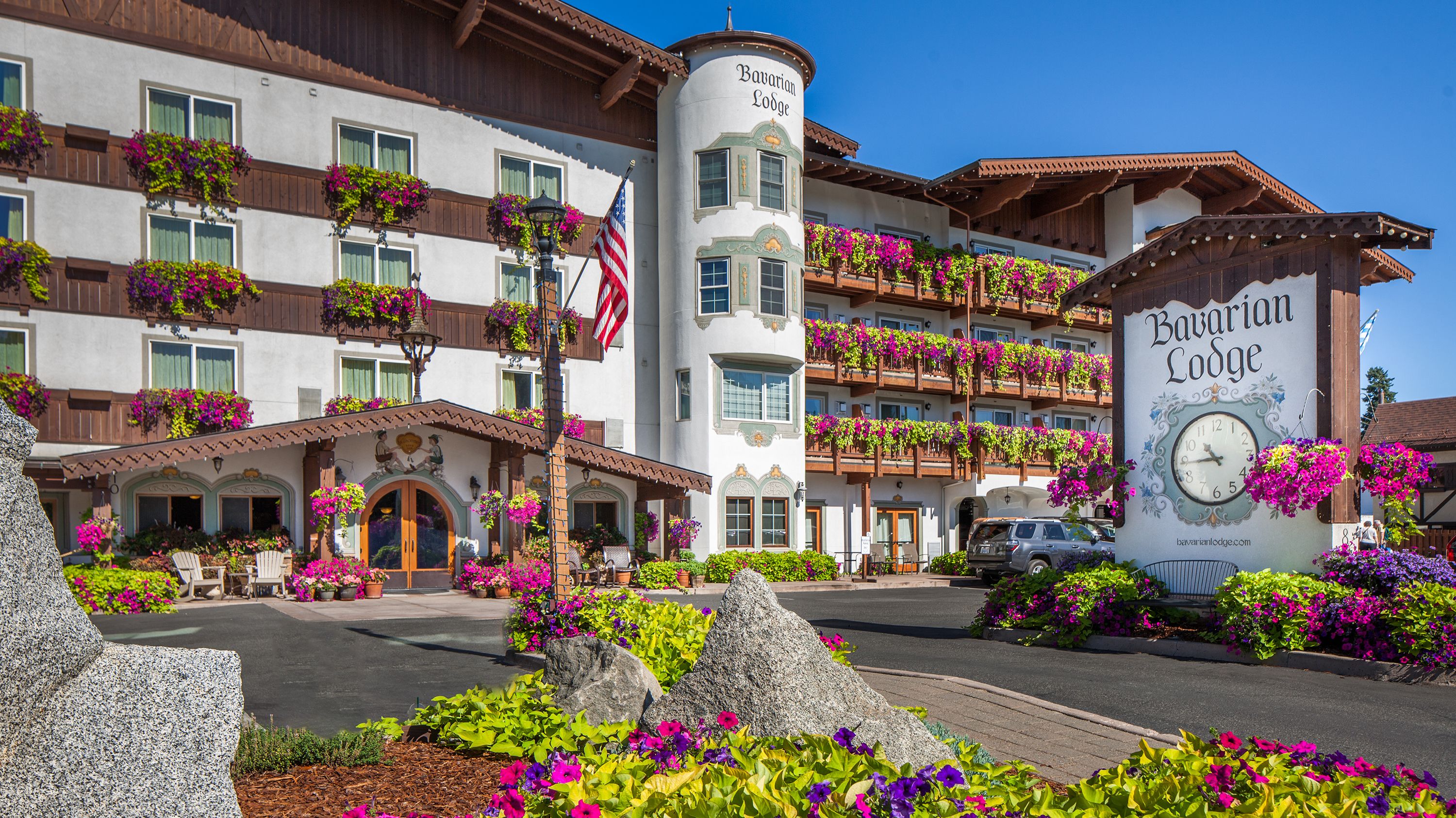 Et bayersk lodge med balkoner pyntet med blomster, et tydeligt ur og en indbydende indgang.