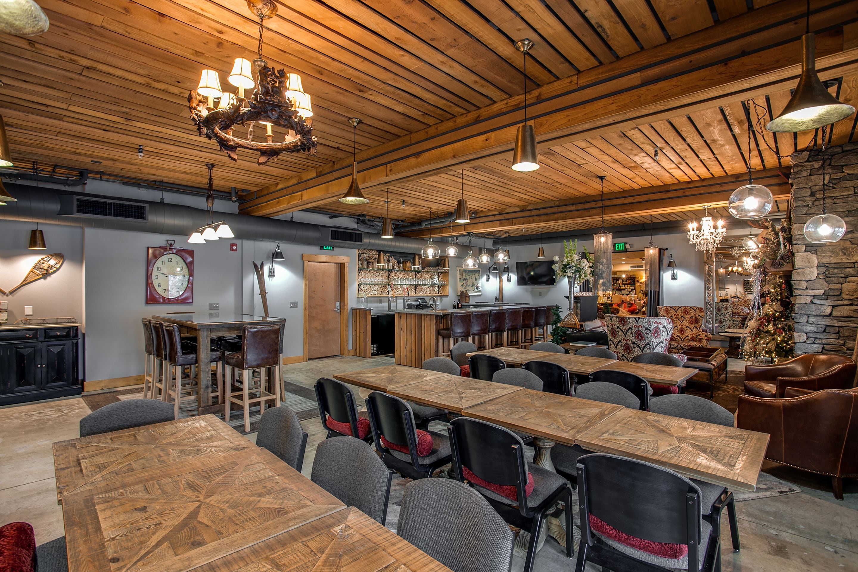 A spacious dining area with long wooden tables and modern chairs, a bar with stools, and a cozy seating area with a Christmas tree.