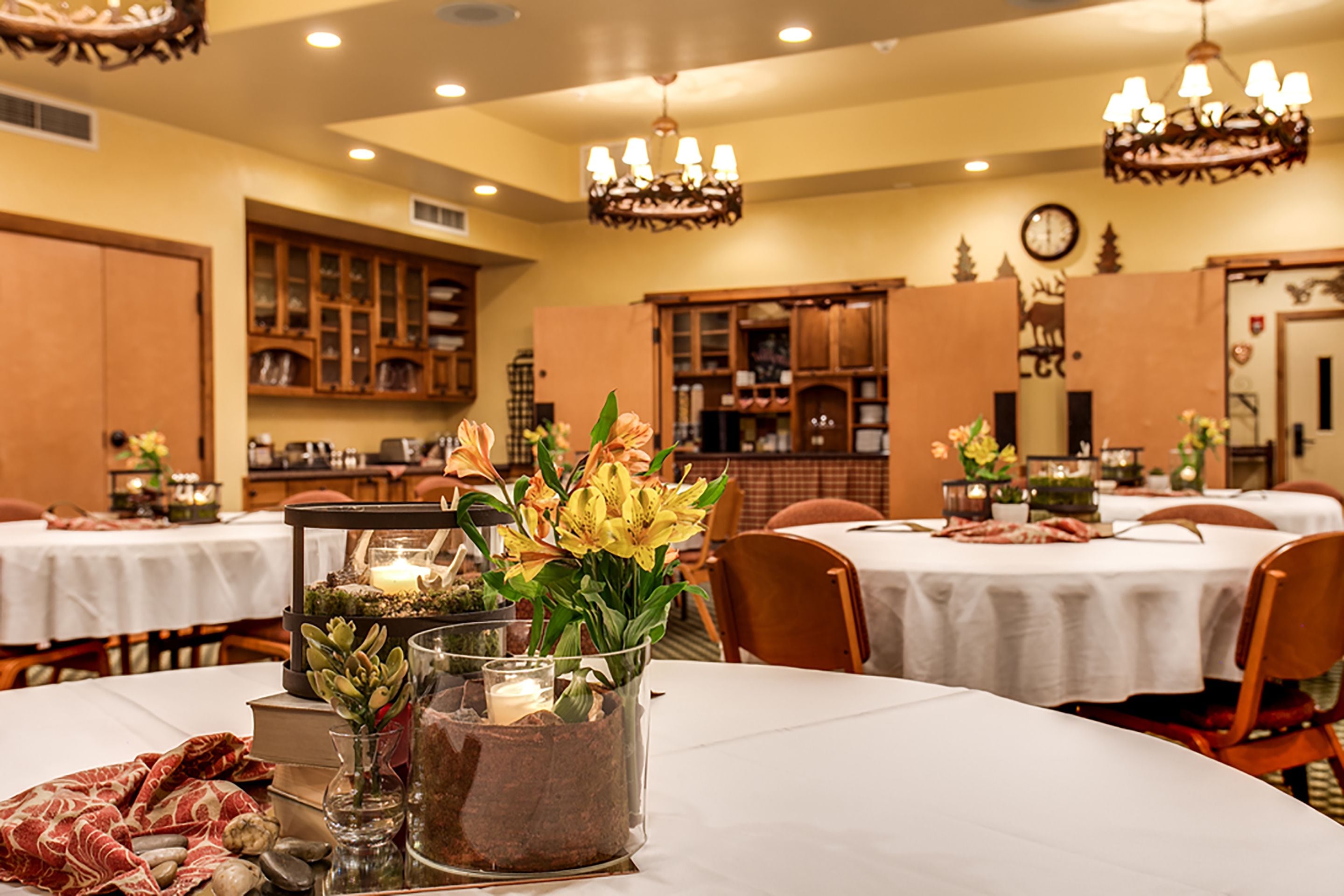Un comedor con mesas redondas, sillas y centros de mesa decorativos que incluyen flores y velas.